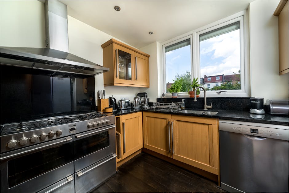 A modern kitchen featuring light wooden cabinetry and a black granite countertop, with a large double-glazed window allowing natural light to illuminate the space. Visible on the countertop are variou